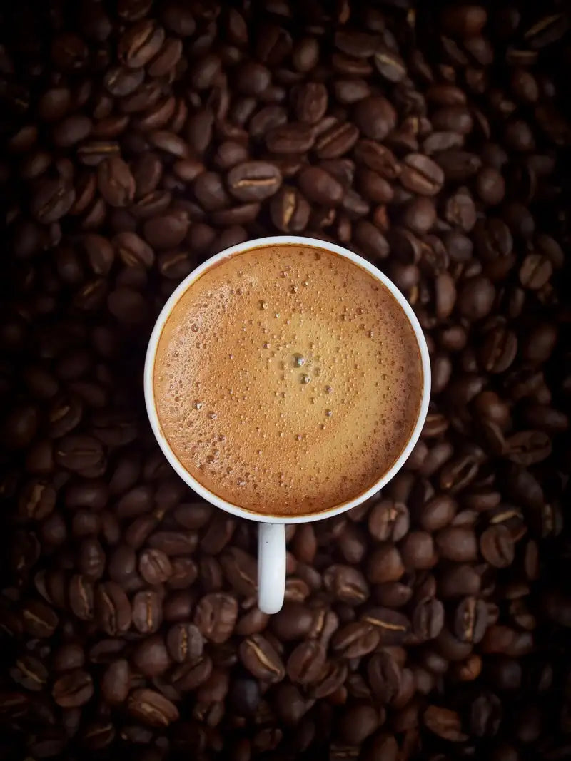 Eine Tasse Kaffee in einem Häufchen Kaffeebohnen, von oben fotografiert.