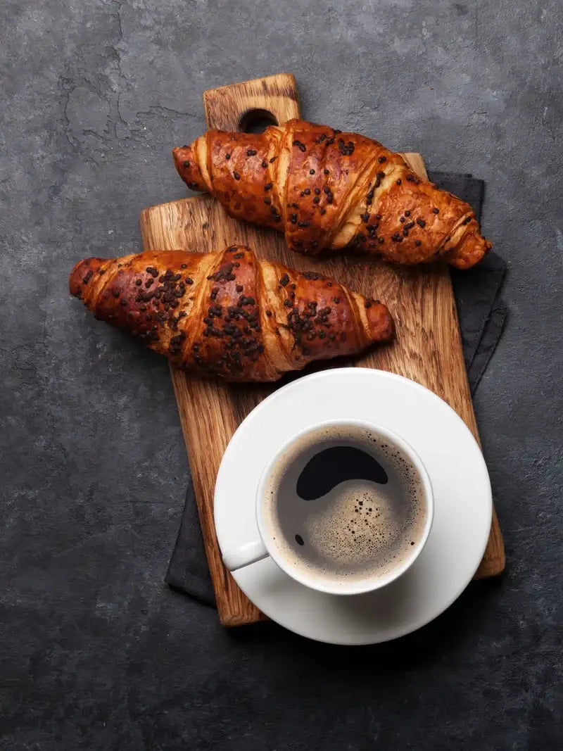 Schoggi-Croissant auf einem Holztablett mit einer Tasse Kaffee.