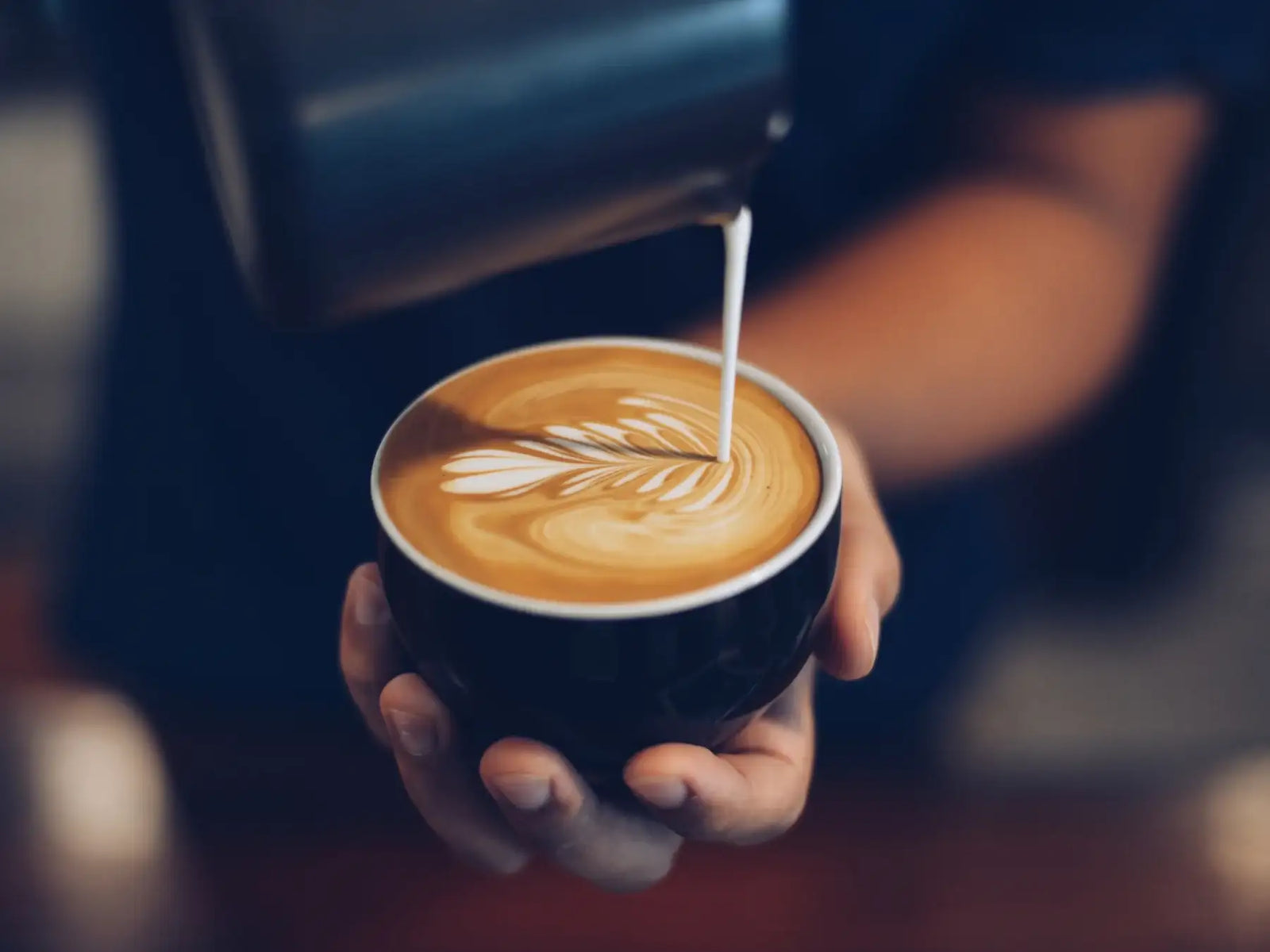 Barista beim Giessen von Latte Art. Warmes Licht.