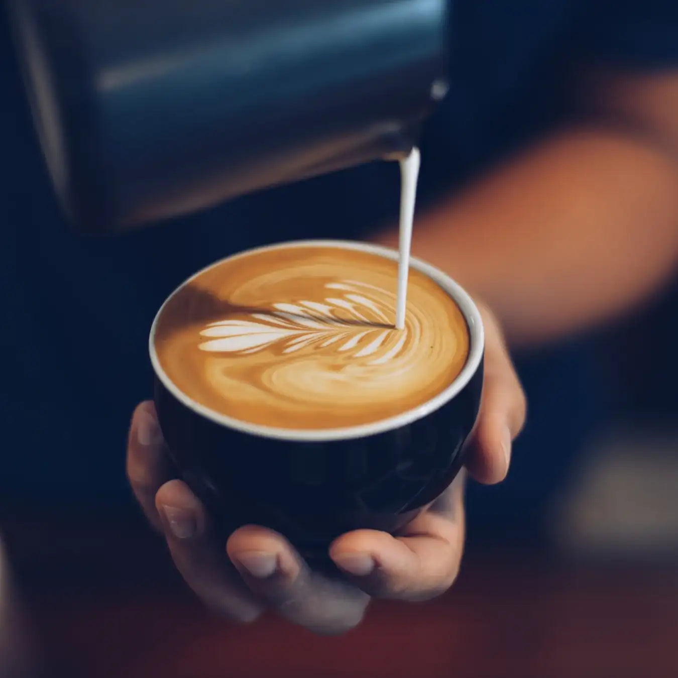 Barista beim Giessen von Latte Art. Warmes Licht